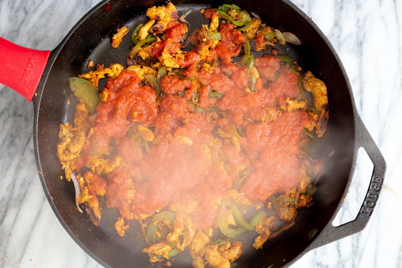 tomato sauce being added to skillet with veggies and soy curls for making Mexican enchiladas