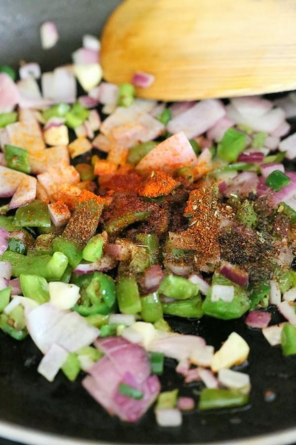 chopped onion, bell peppers, chili and garlic powder being sauteed in a black pan