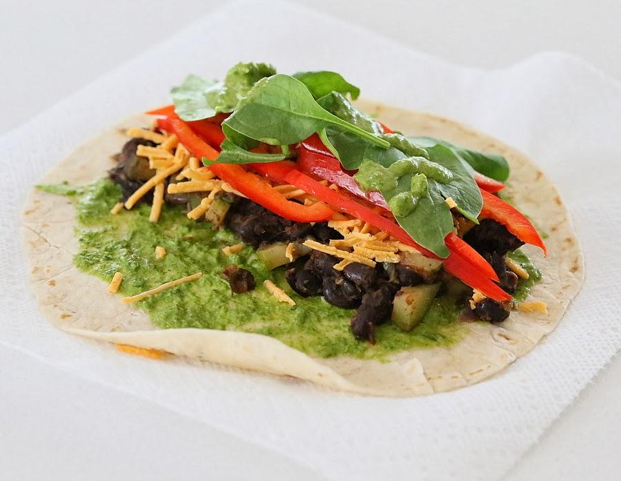 a wheat tortilla wrap topped with black beans, spinach and dairy-free cheese