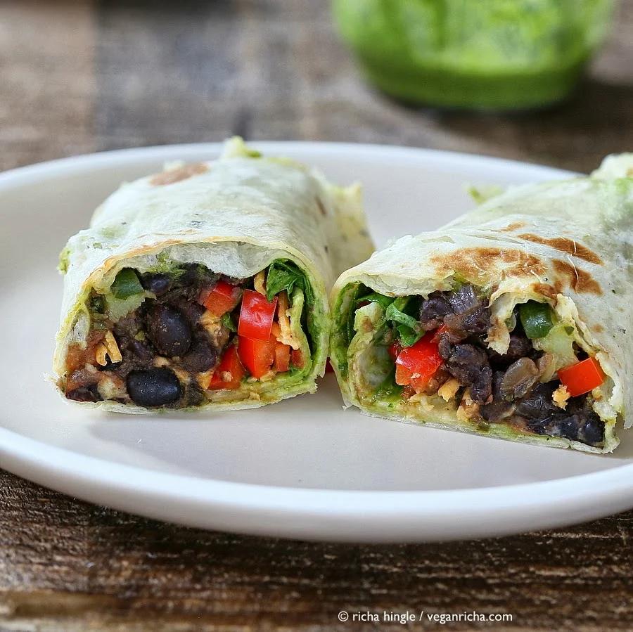 a halved healthy vegan wrap with smoky black beans, spinach, chimichurri and vegan cheese on a white plate