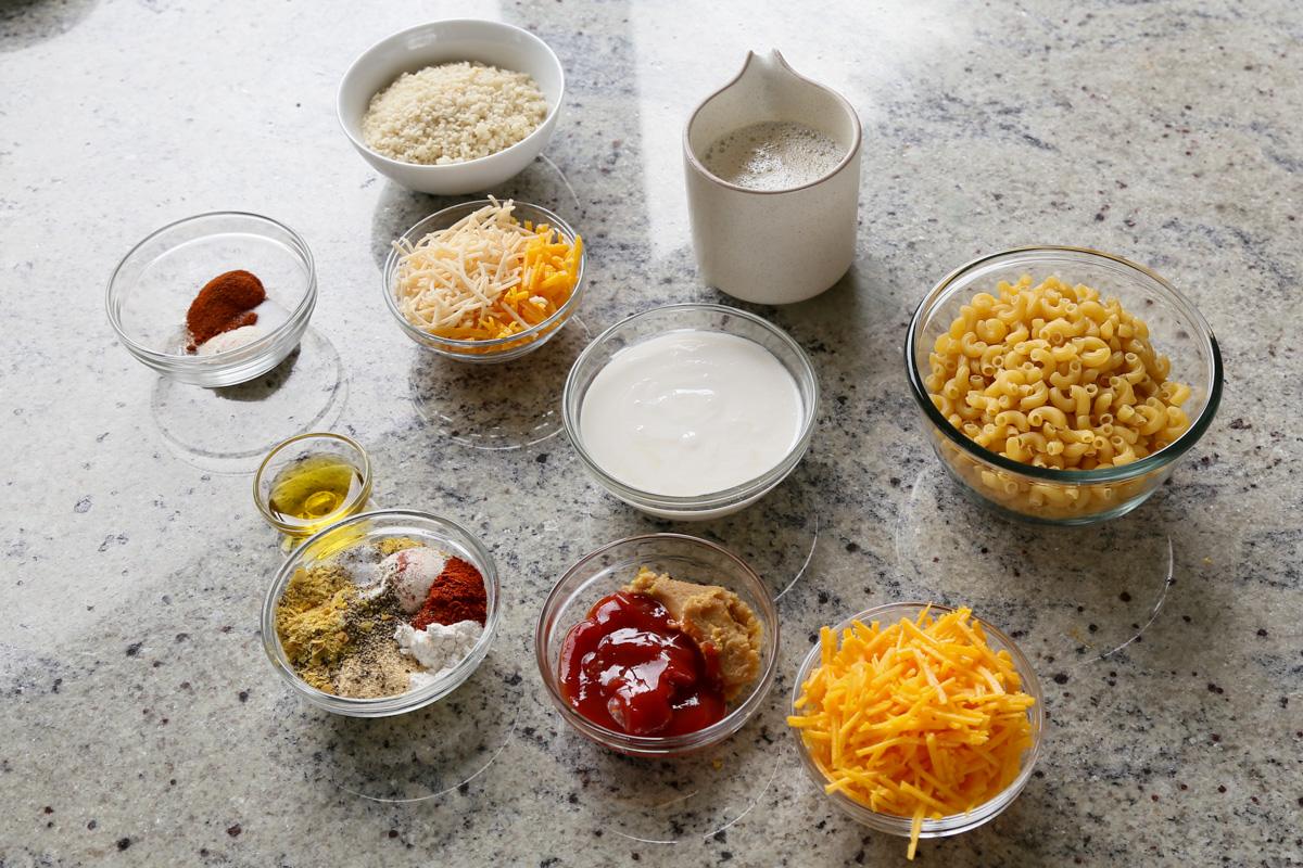 pasta, vegan cheese, and other mac and cheese ingredients in bowls on the kitchen counter
