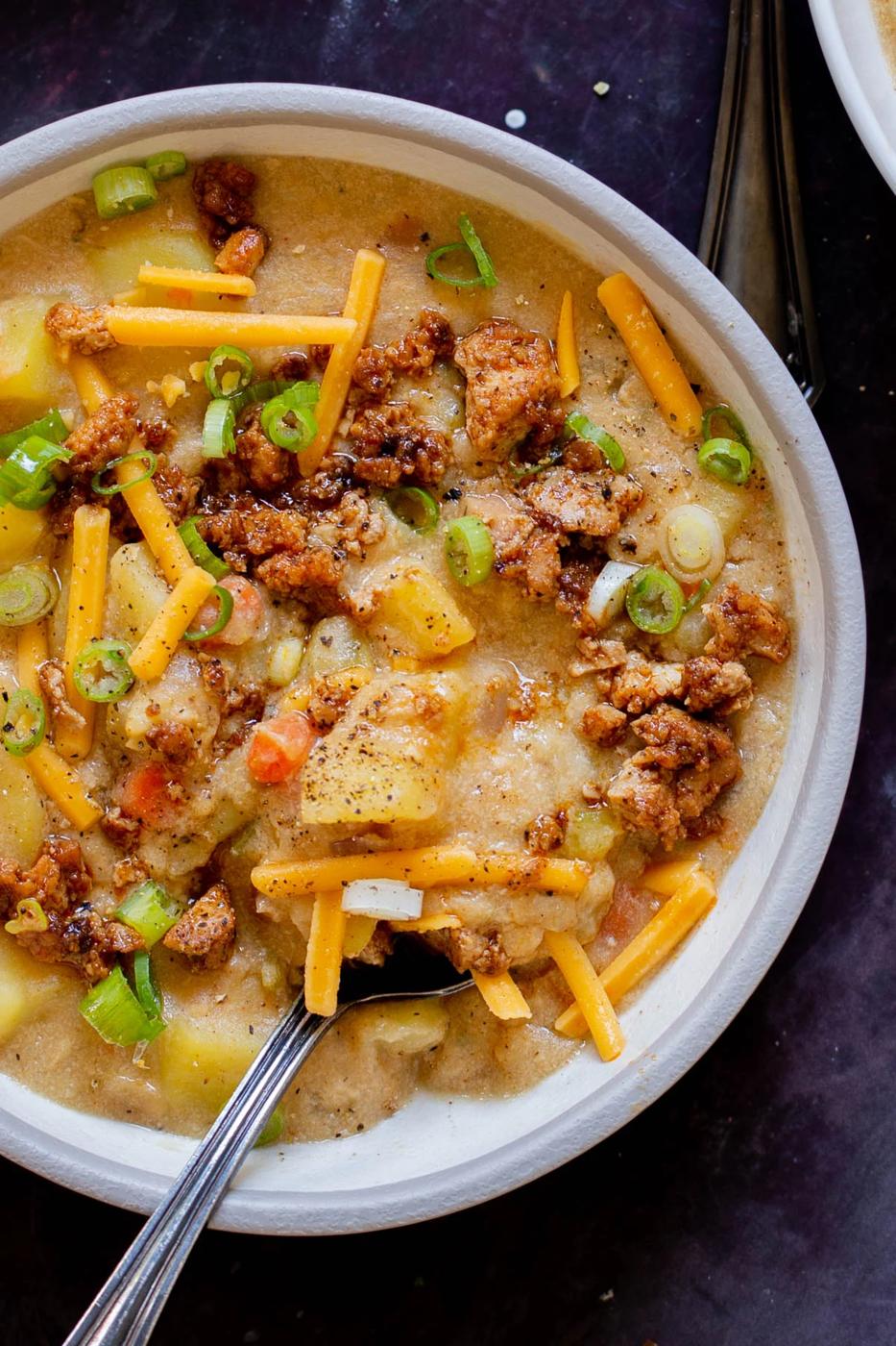 bowl of smoky vegan potato soup topped with tofu crumbles, green onions, and vegan cheese