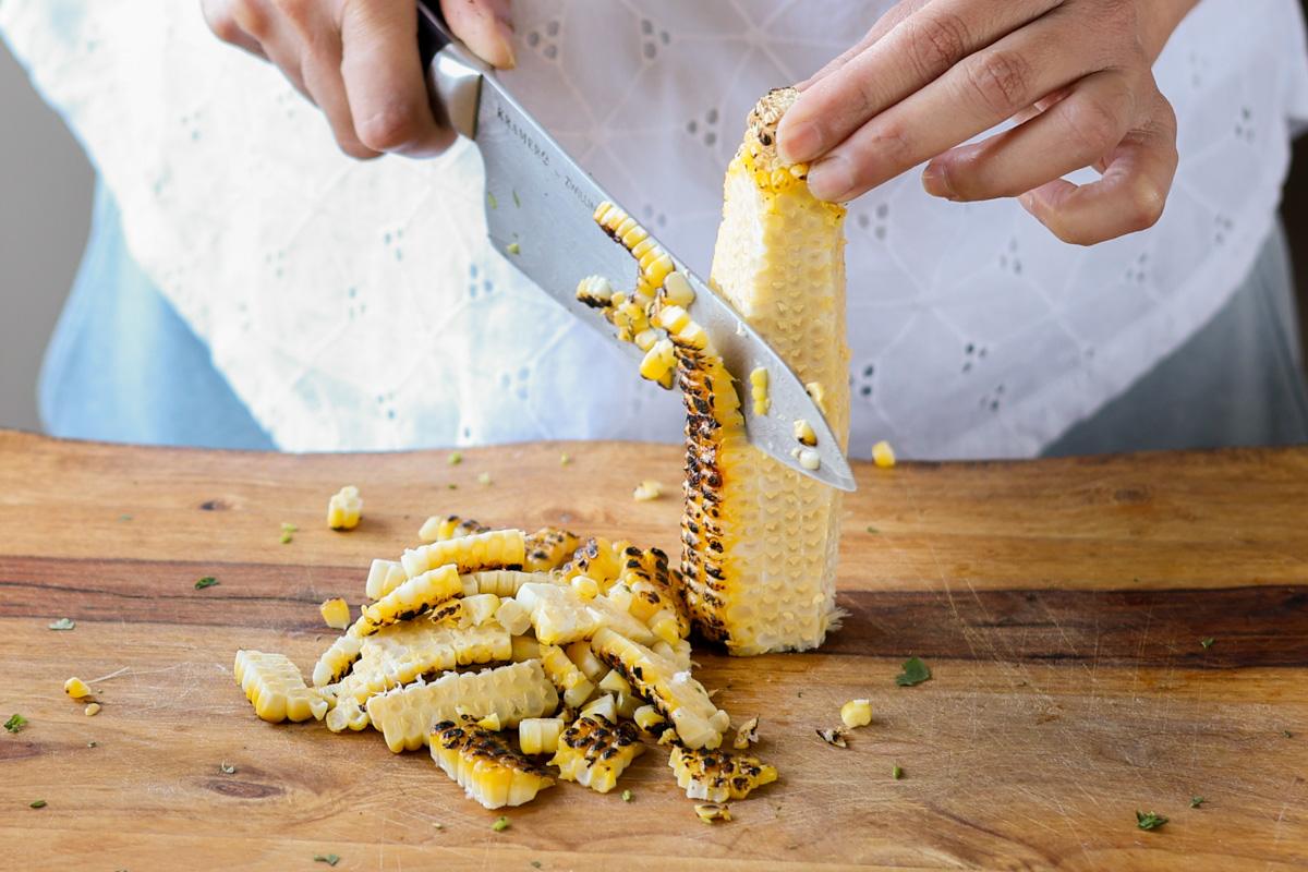 A knife sliding down the side of the corn taking off the kernels.