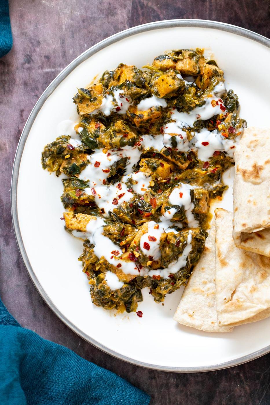 a serving of spinach tofu curry drizzled with yogurt and served with flatbread