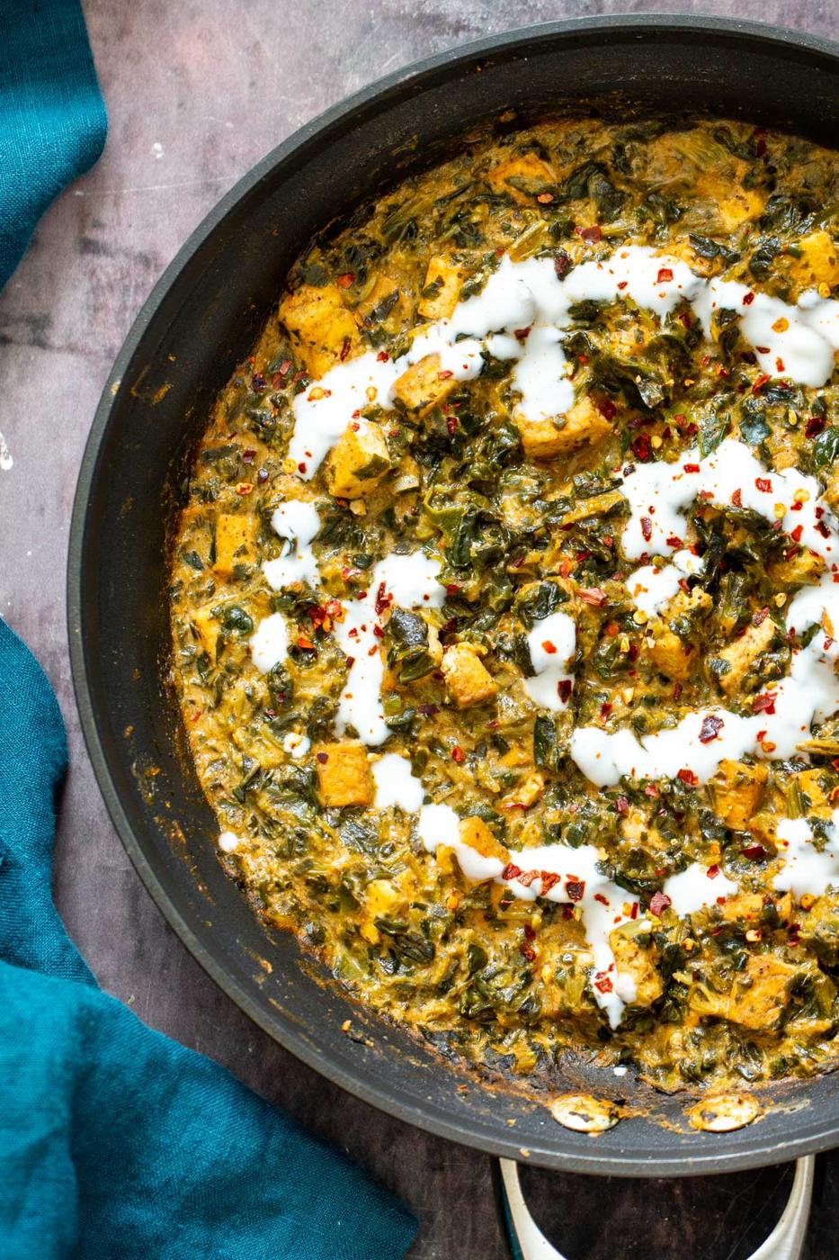 a skillet with spinach tofu curry drizzled with yogurt