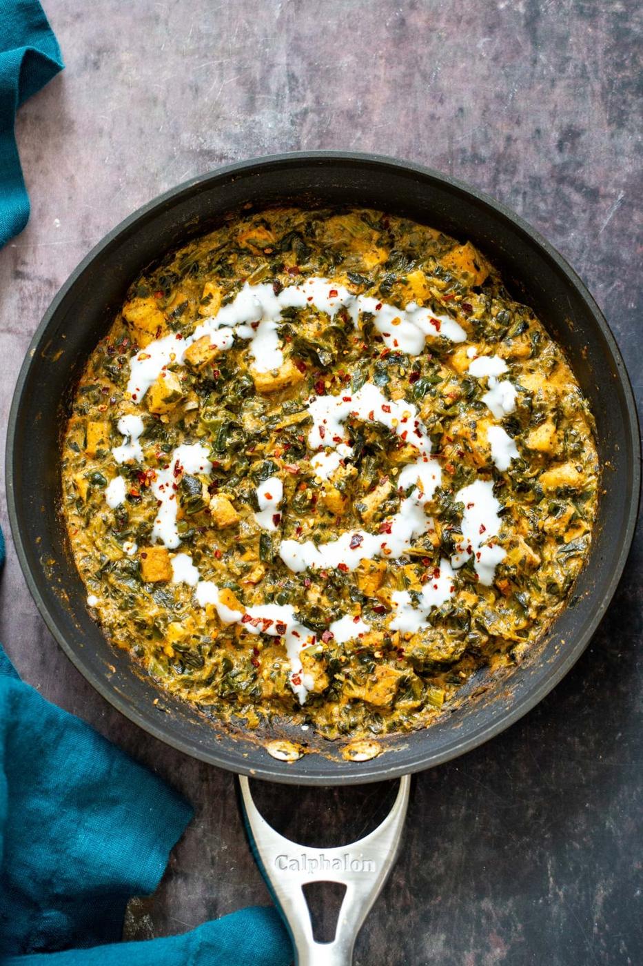 a skillet with spicy vegan spinach tofu curry drizzled with vegan yogurt