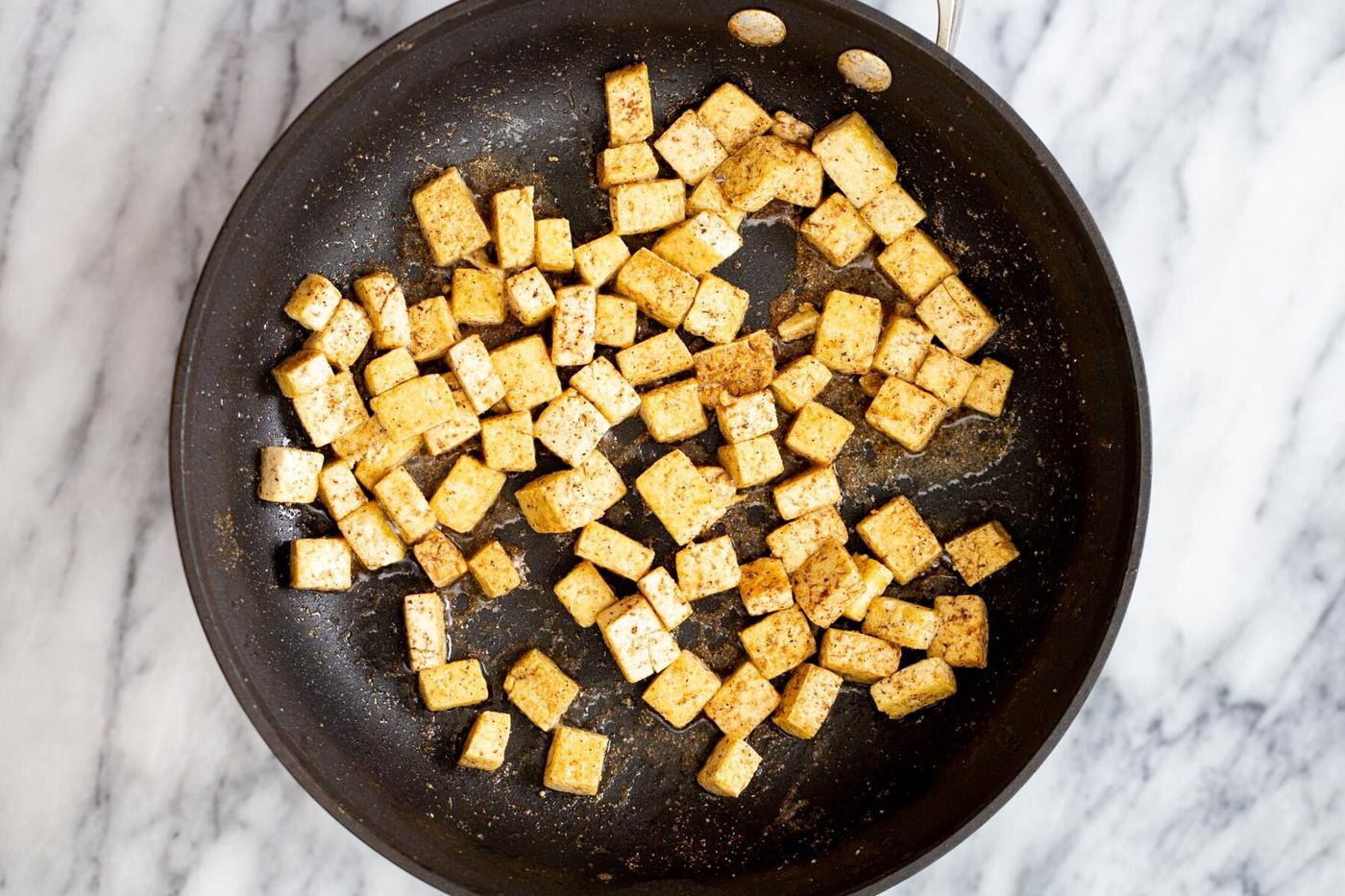 tofu cubes frying in a black skillet
