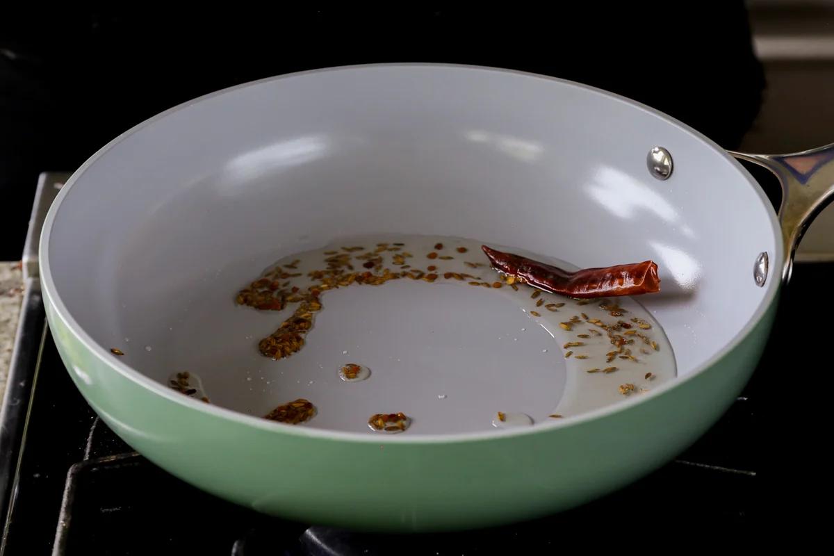 adding a red chili to the pan of roasted spices