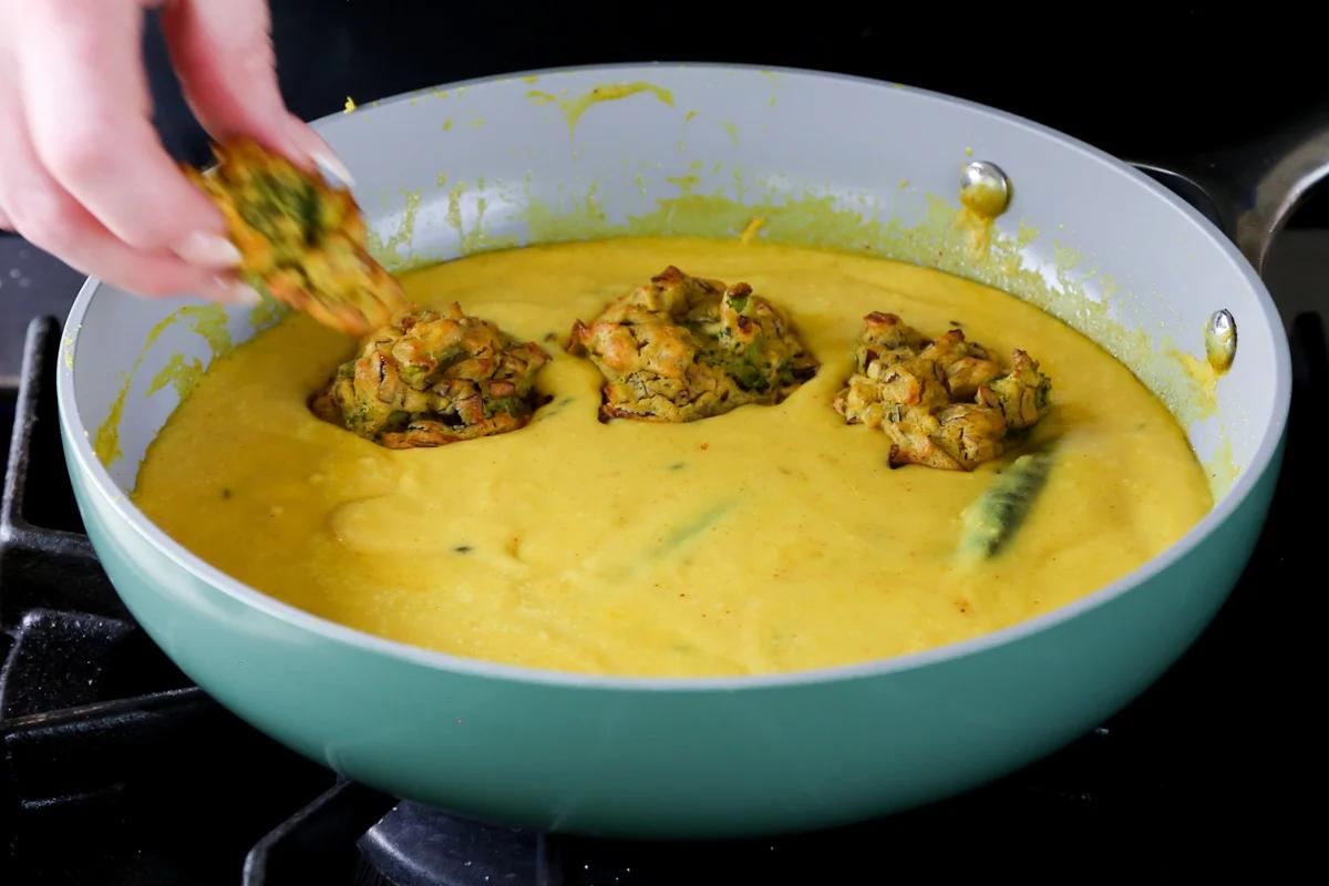 adding pakora to the pan of curry sauce