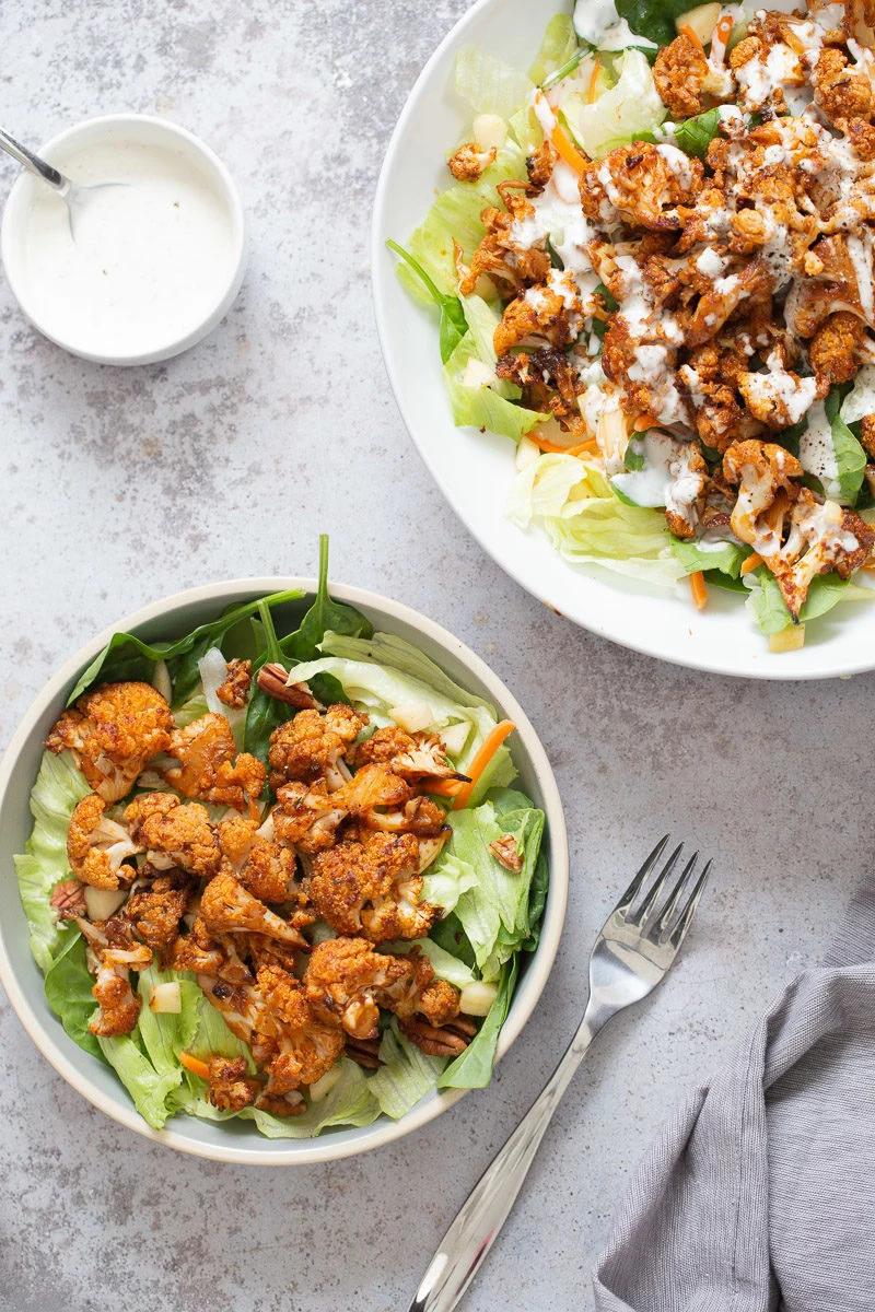 overhead shot of a spicy bbq roasted cauliflower salad bowl in a white bowl drizzled with Vegan Ranch Dressing ” width=