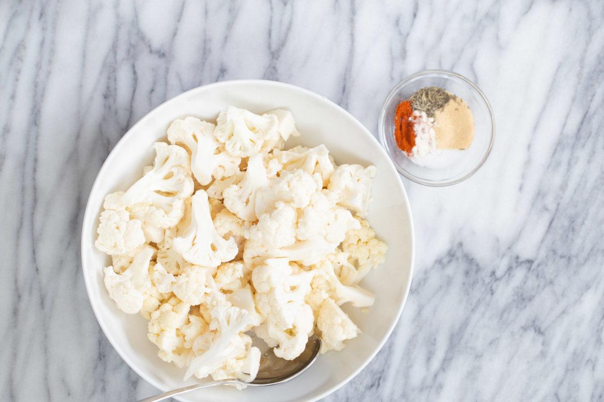 cauliflower florets in a white bowl next to a side dish with bbq spices