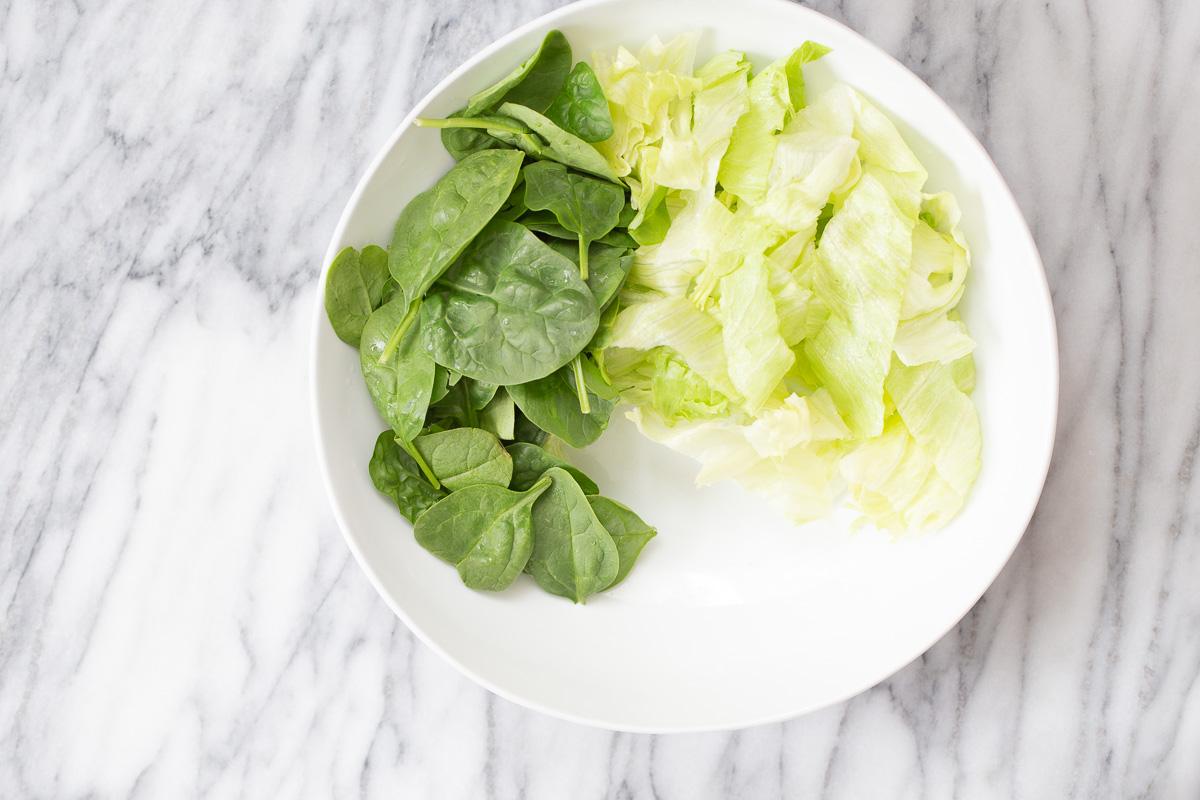 spinach and iceberg salad being arranged in a white bowl to make cauliflower salad bowl