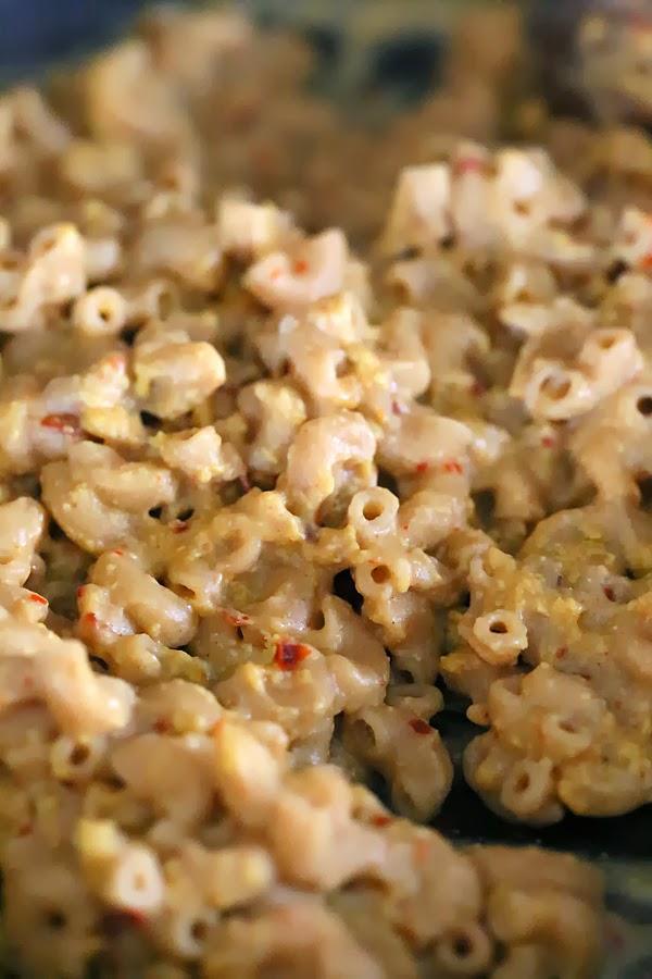 whole wheat elbow pasta being tossed with dairy-free cheese sauce to make vegan mac and cheese