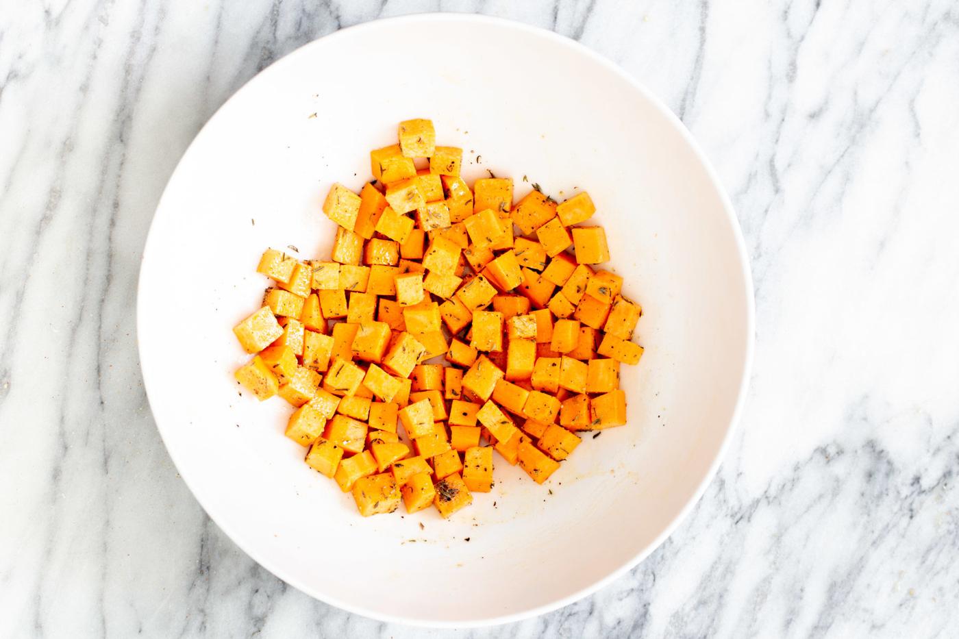 sweet potato cubes mixed with seasoning and oil in a small bowl