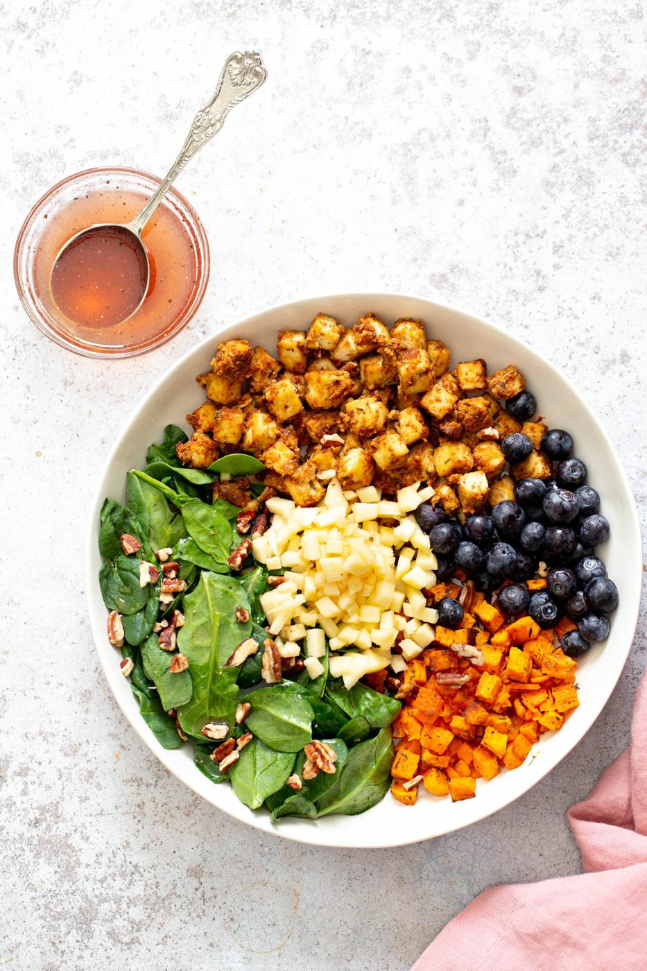 all ingredients for sweet potato tofu bowls assembled in a shallow white bowl with a side dish with dressing