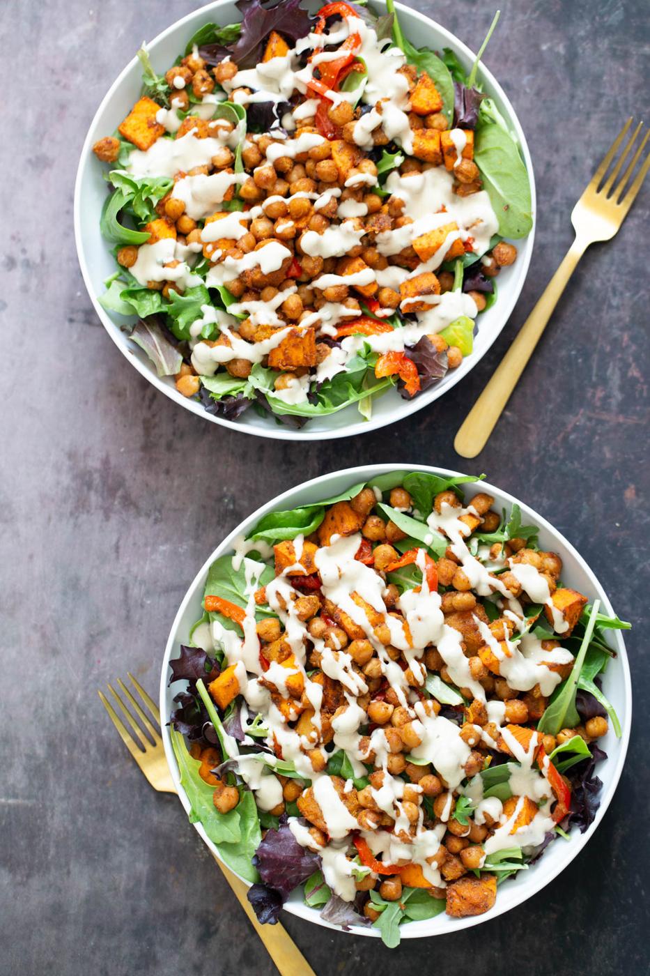 sweet potato chickpea salad served in two white bowls drizzled with tahini dressing