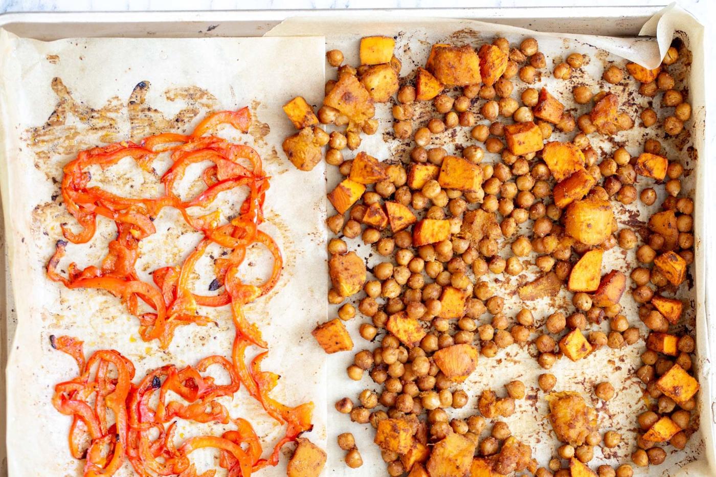 chickpeas, sweet potatoes and sliced red bell peppers being baked on a sheet pan for vegan salad bowl recipe