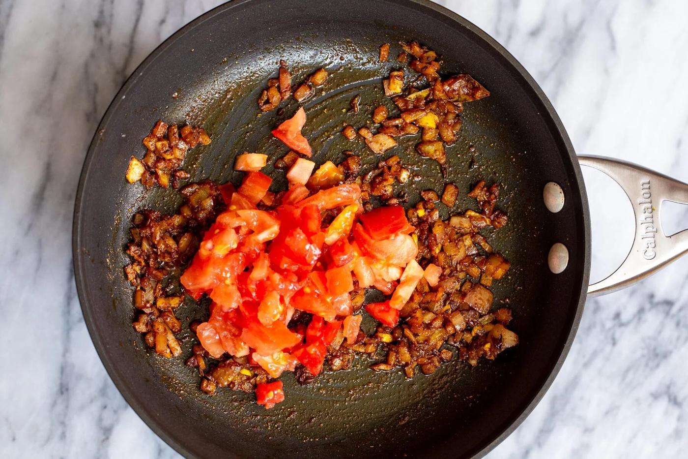 fresh tomatoes being added to skillet with onions and spices