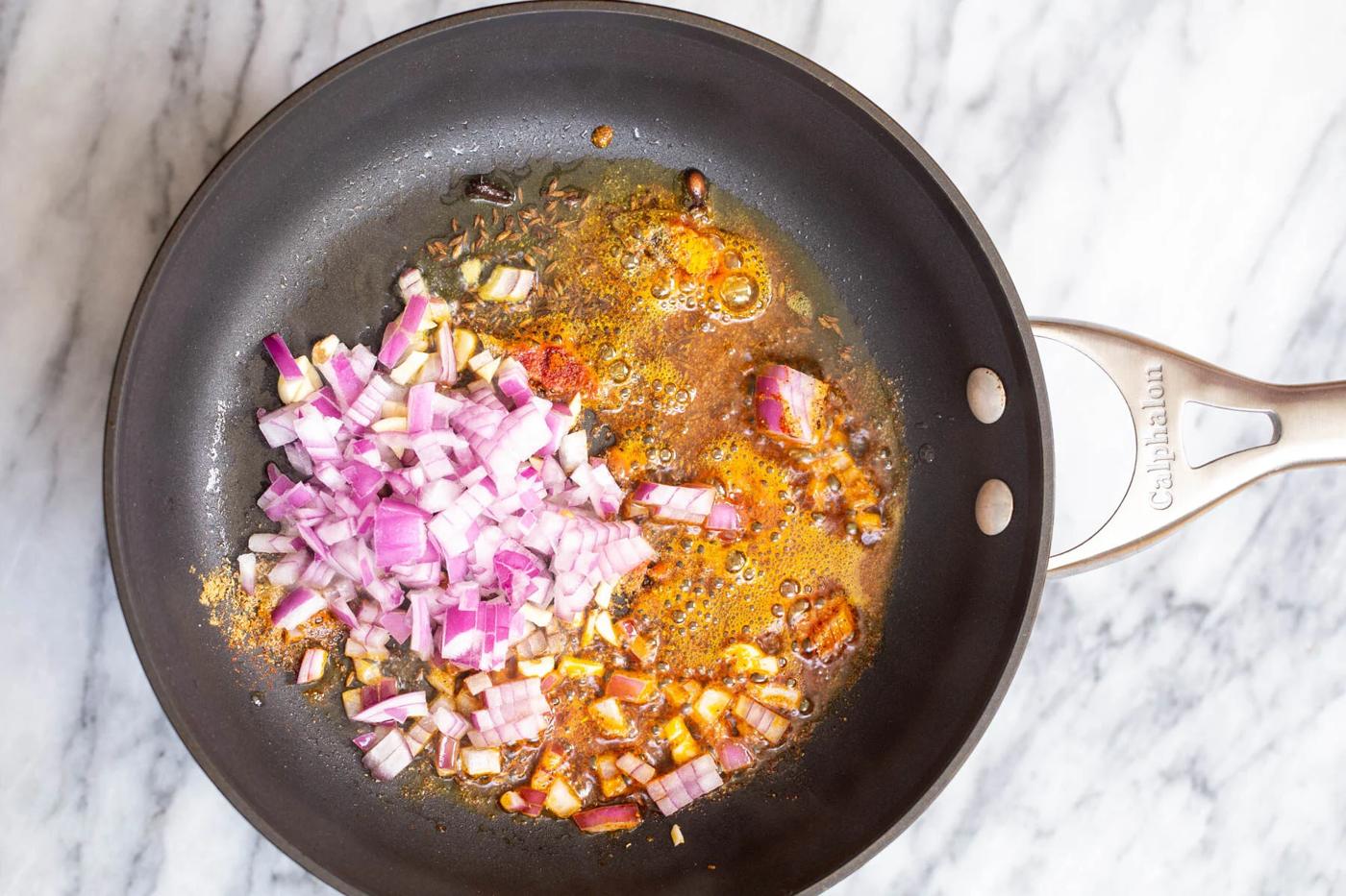 chopped red onion being added to tempering to make ural dal