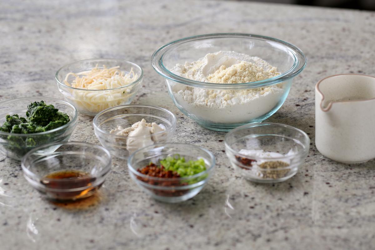 flour, spinach, cheese, and other scones ingredients in bowls on the kitchen counter