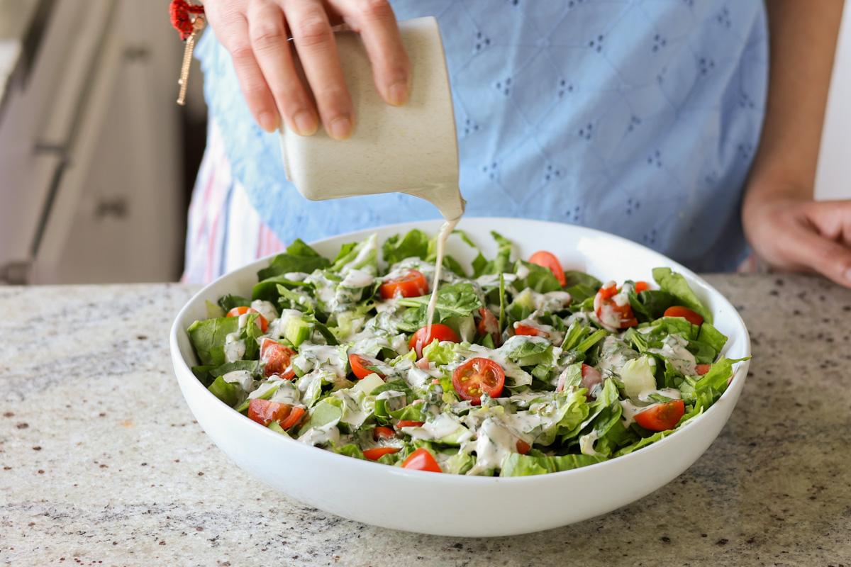 pouring the tahini dressing onto the spinach salad