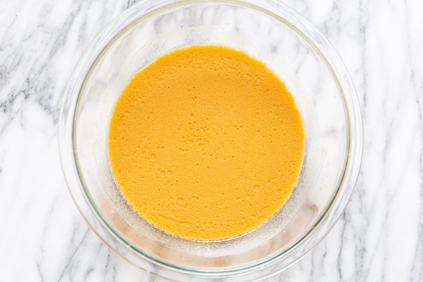 wet ingredients for sweet potato cinnamon rolls being mixed in a glass bowl
