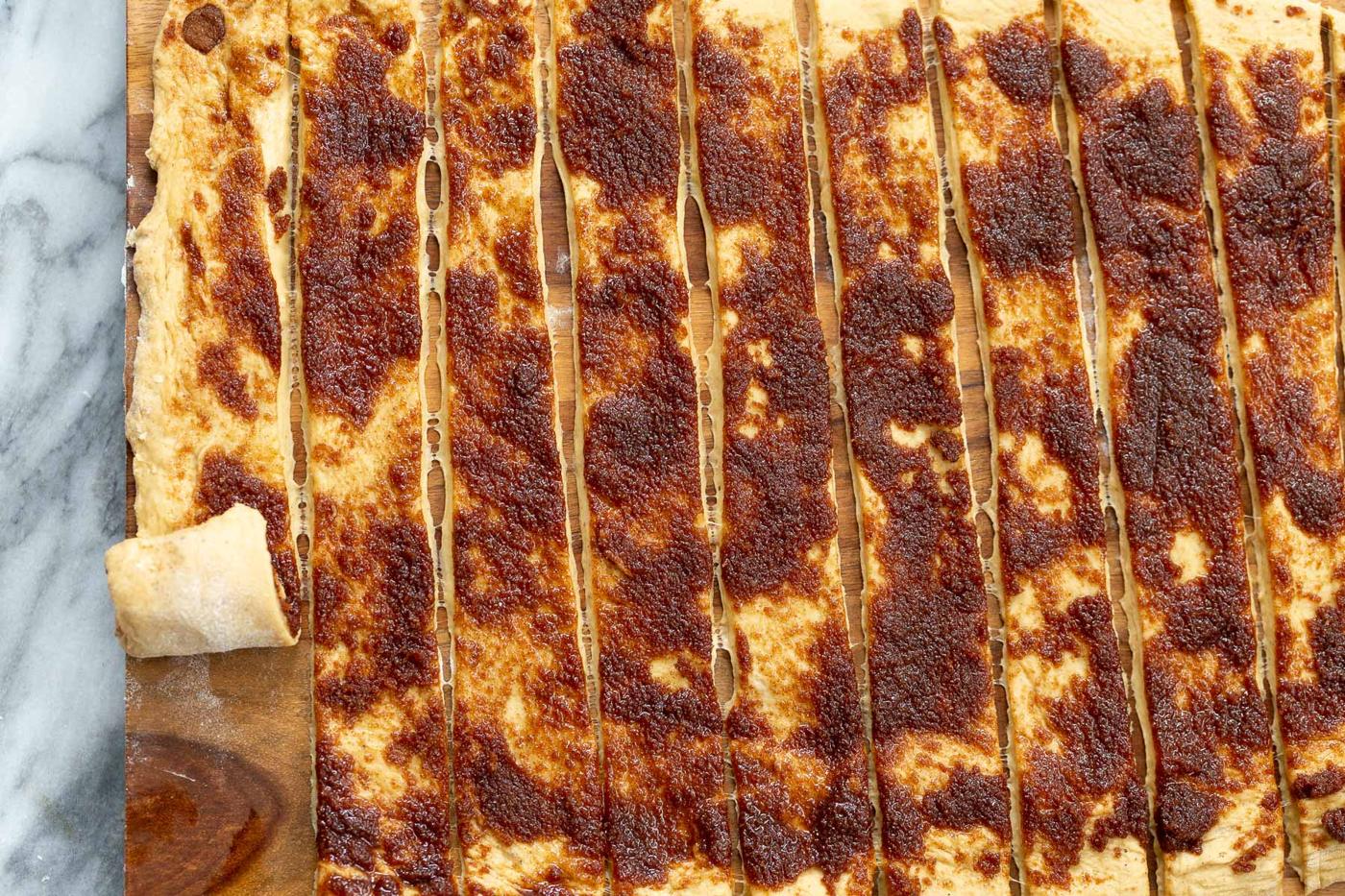 rolled out cinnamon rolls dough being cut into strips and rolled up into buns