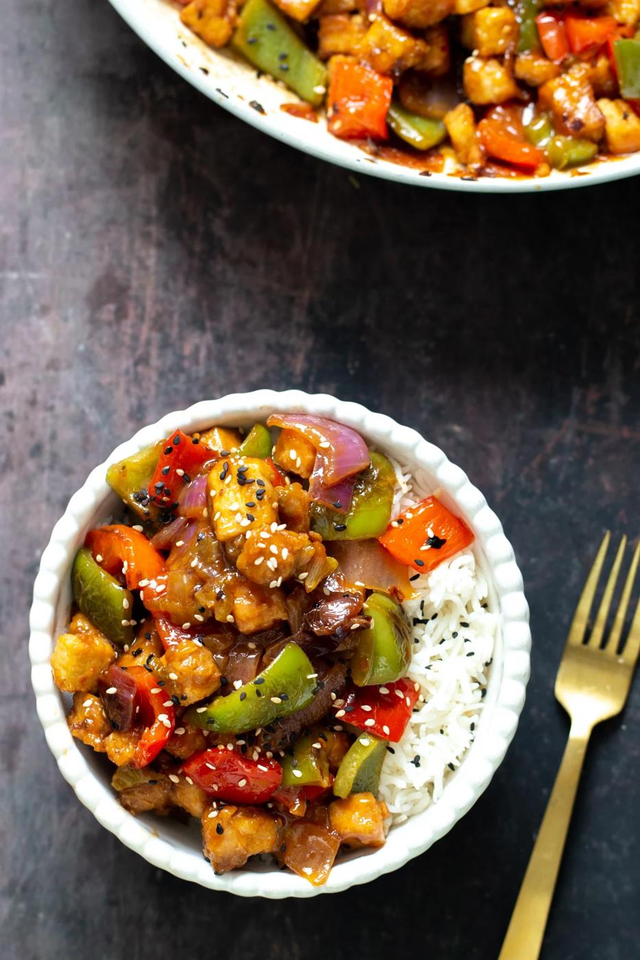 sweet and sour tofu stir-fry with rice served in a white bowl with a fork on the side