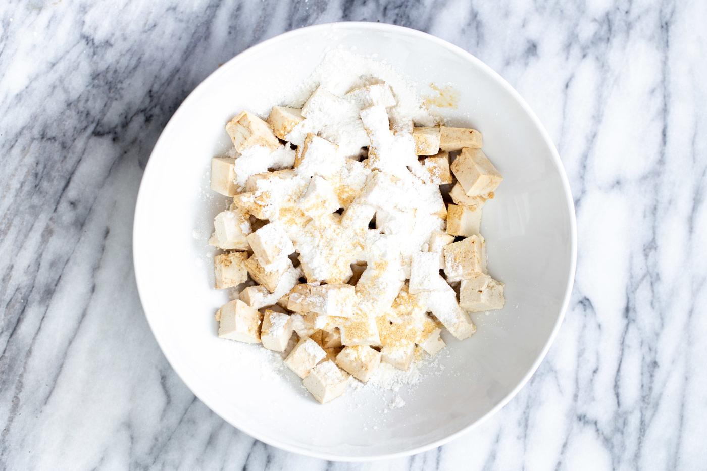 marinated tofu cubes being tossed with cornflour in a bowl