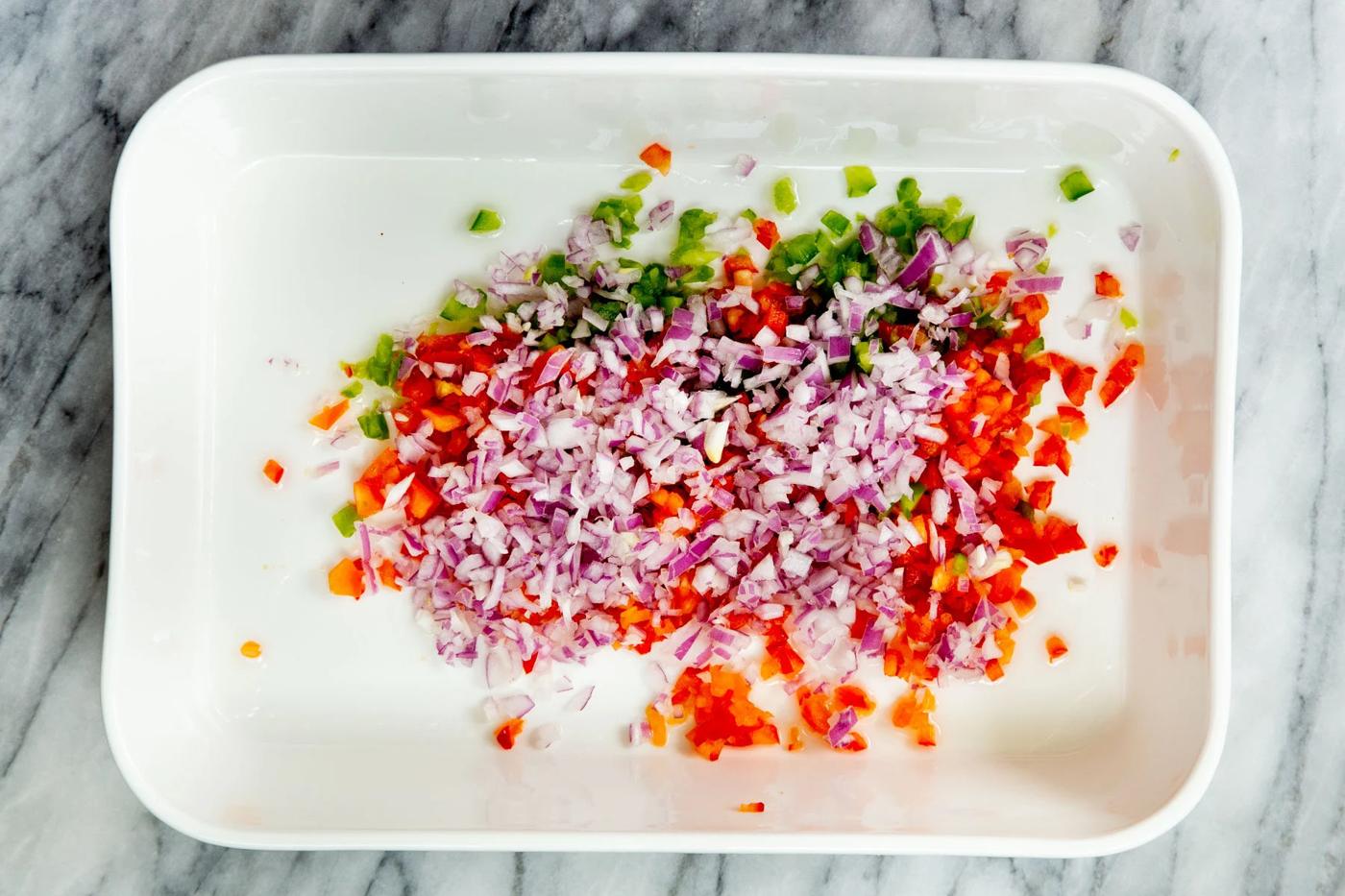 chopped onions and bell pepper in a white casserole dish