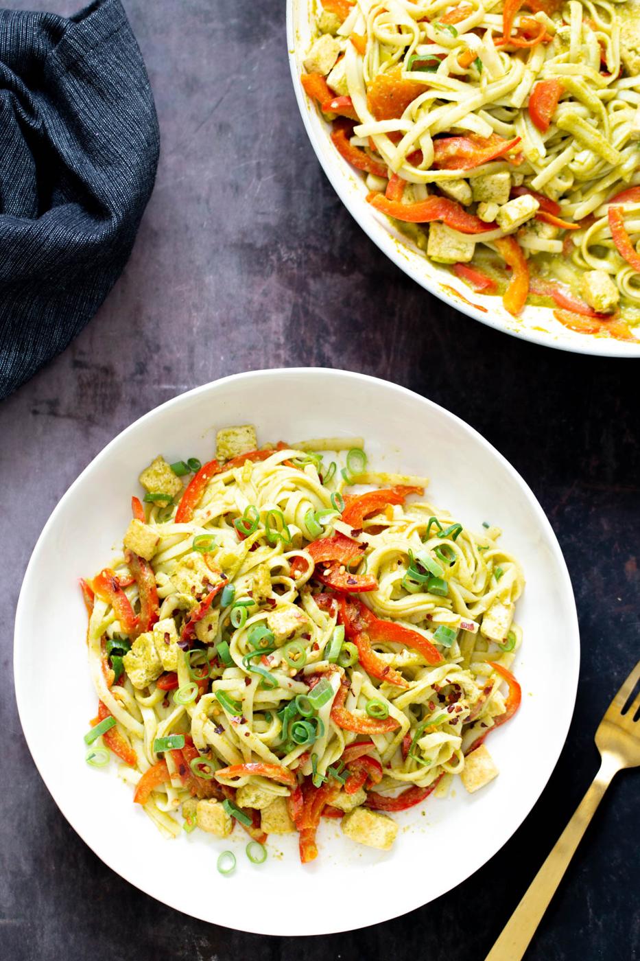 two servings of Thai green curry noodles with bell peppers and green onion with a fork on the side