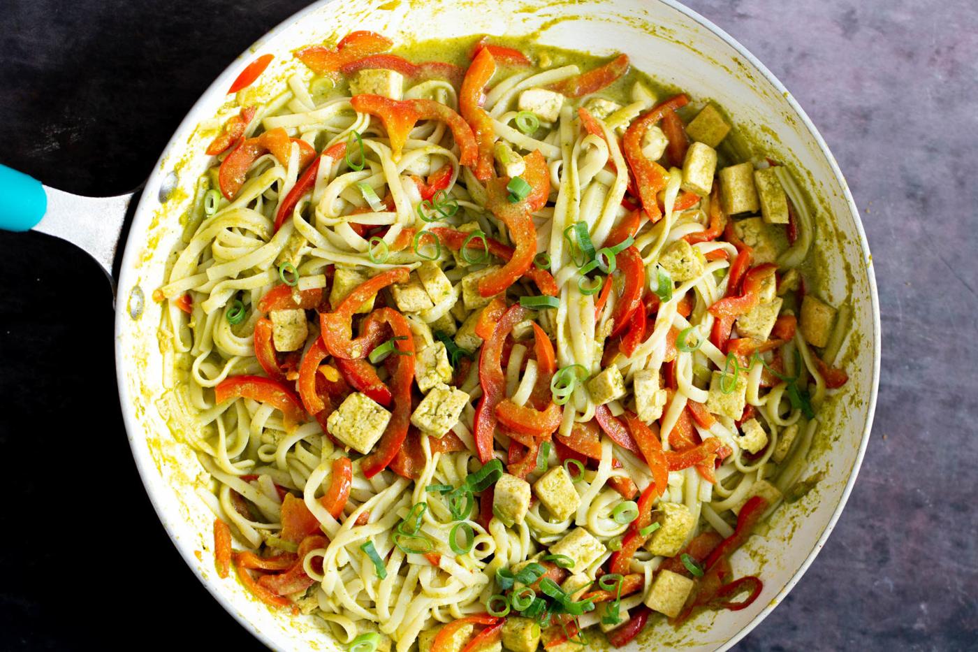 rice noodles being tossed in a pan with sauteed veggies, tofu and green curry sauce