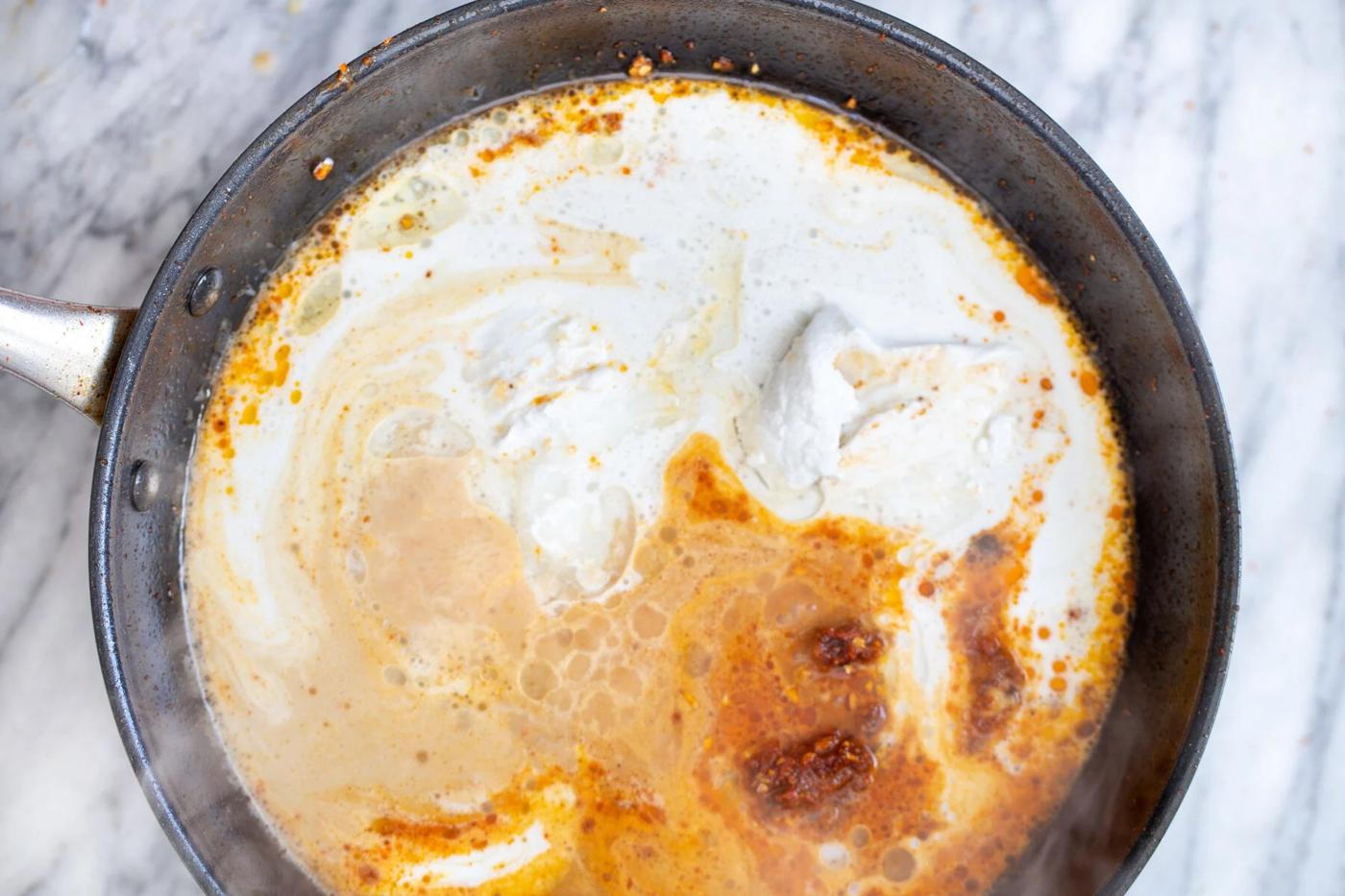 coconut milk being added to thai curry in a saucepan