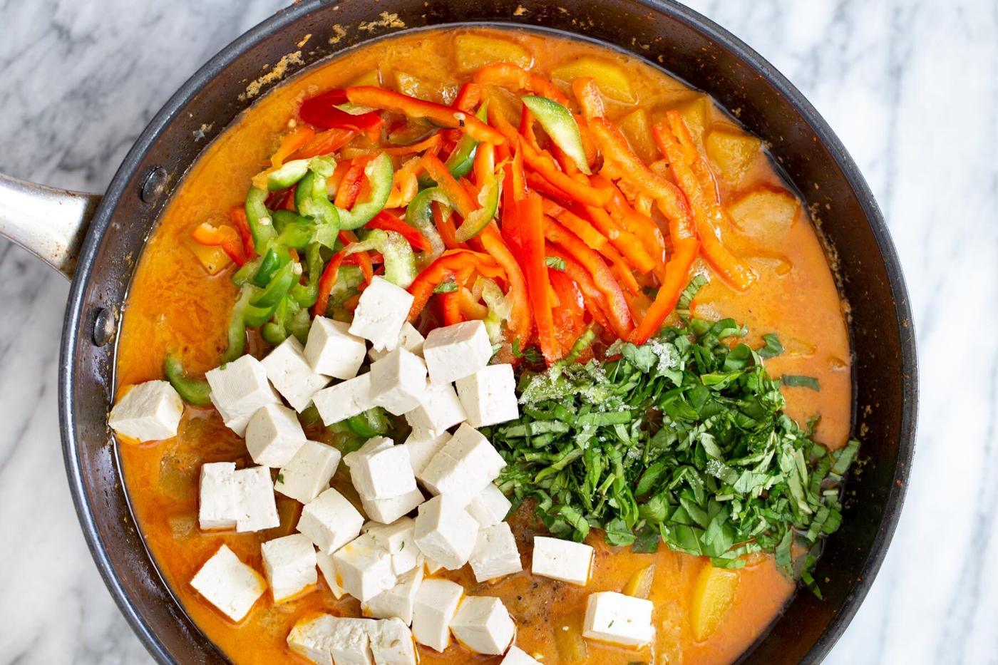 tofu and veggies being added to coconut broth in a saucepan