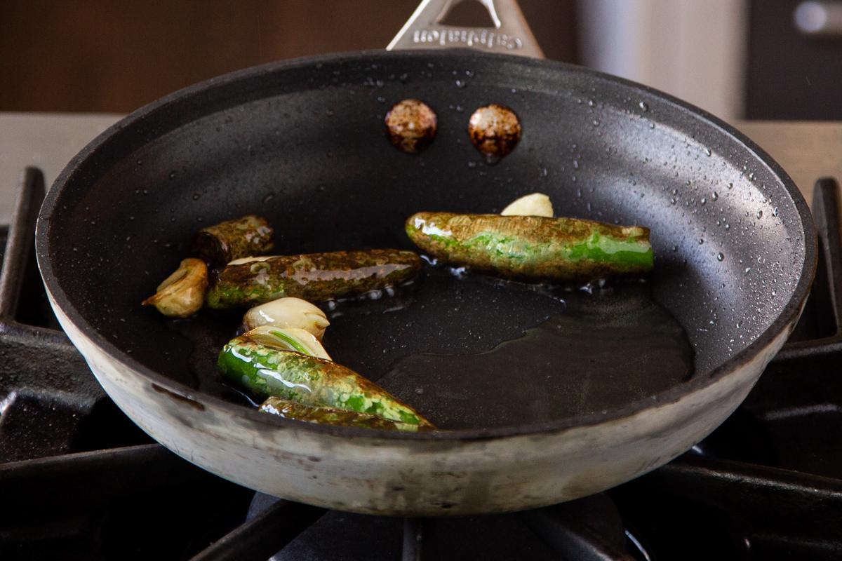 adding garlic to the pan of blistered chilis