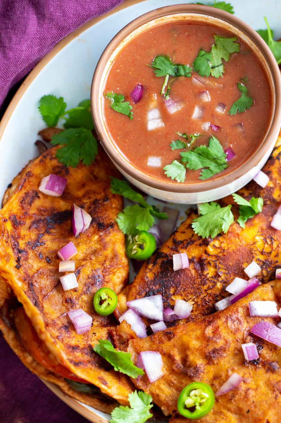 a plate of vegan birria tacos with a side dish of masala sauce
