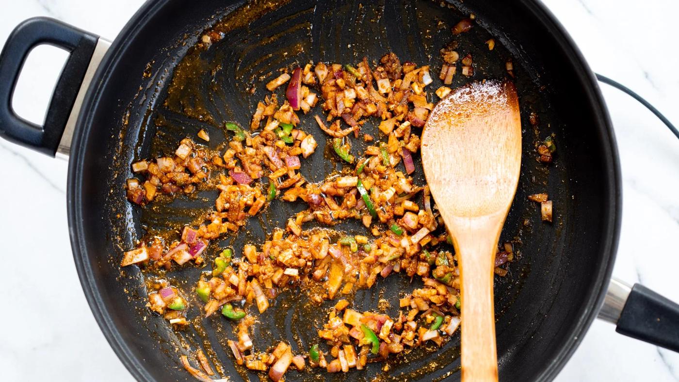 Our Vegan Tofu Amritsari Masala Sauce step with spices and onion getting cooked in a black skillet