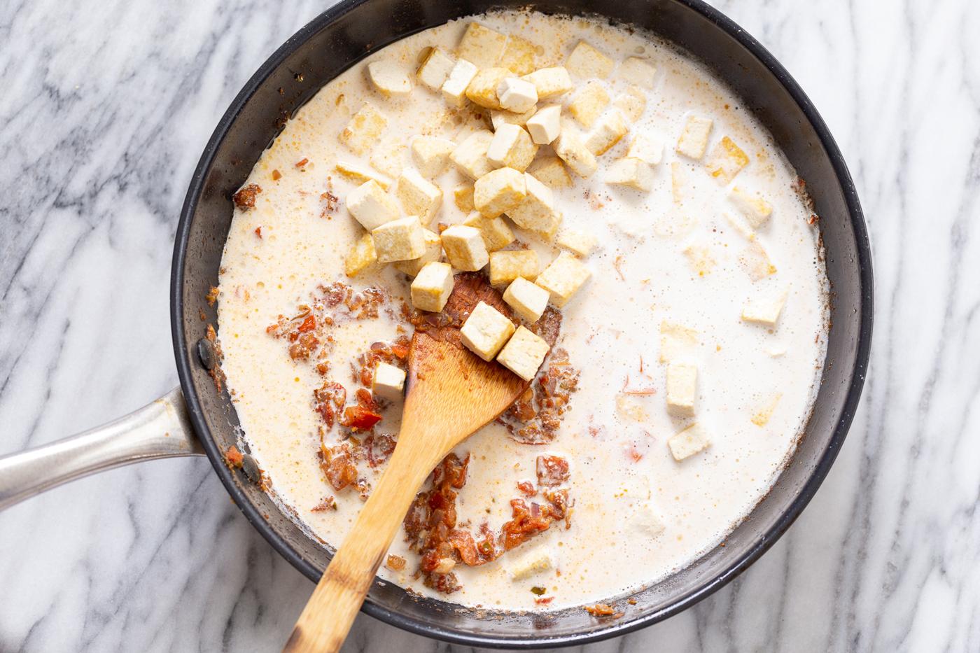 tofu cubes and cashew cream being added to skillet to make creamy Indian tofu curry
