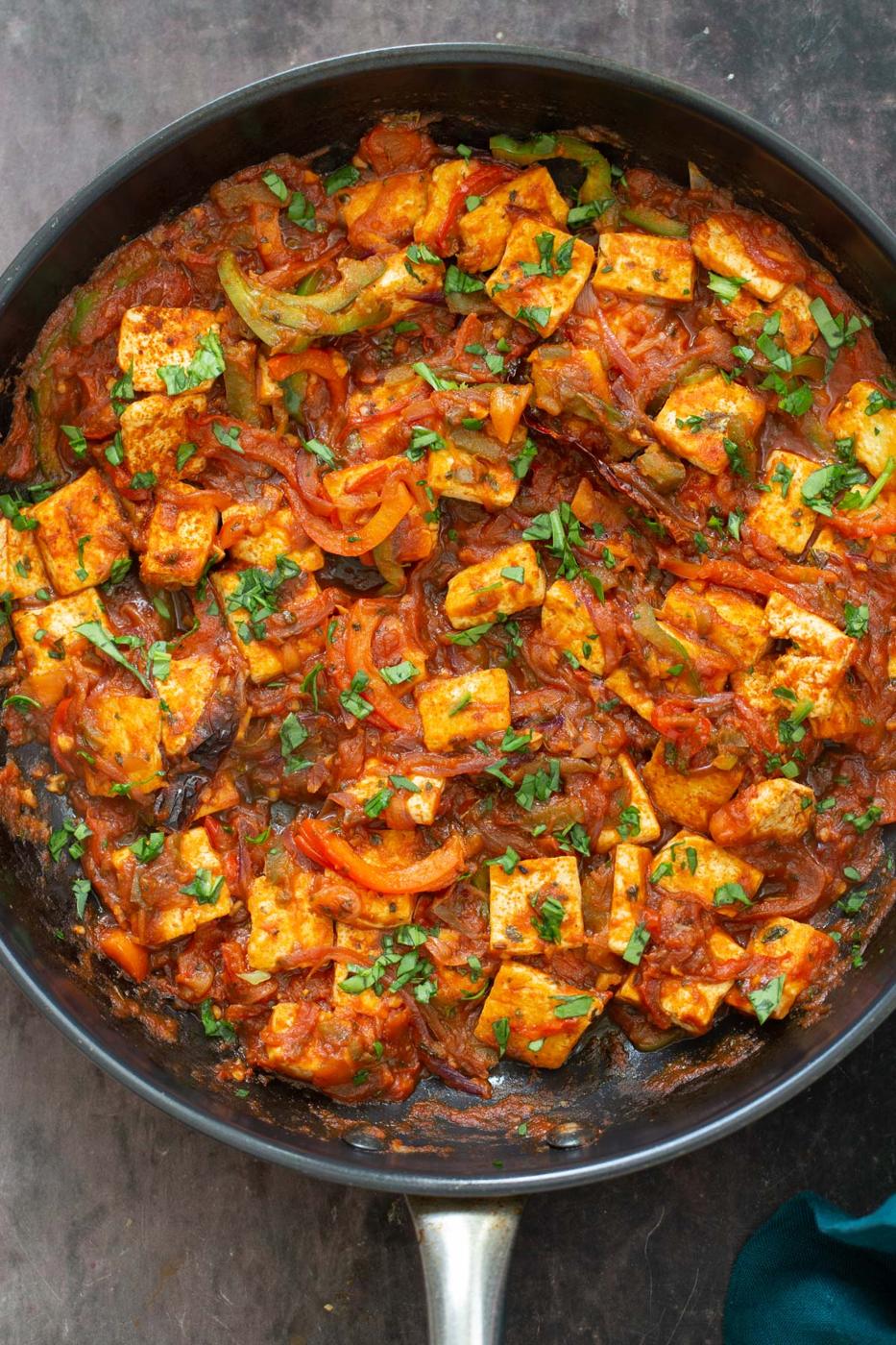 a black skillet with tofu in jalfrezi sauce sprinkled with cilantro