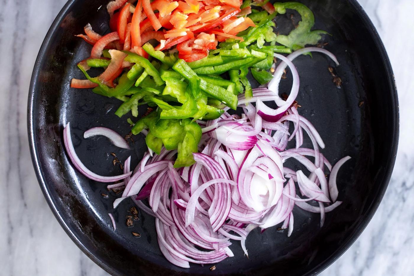 sliced bell peppers and onions being added to skillet