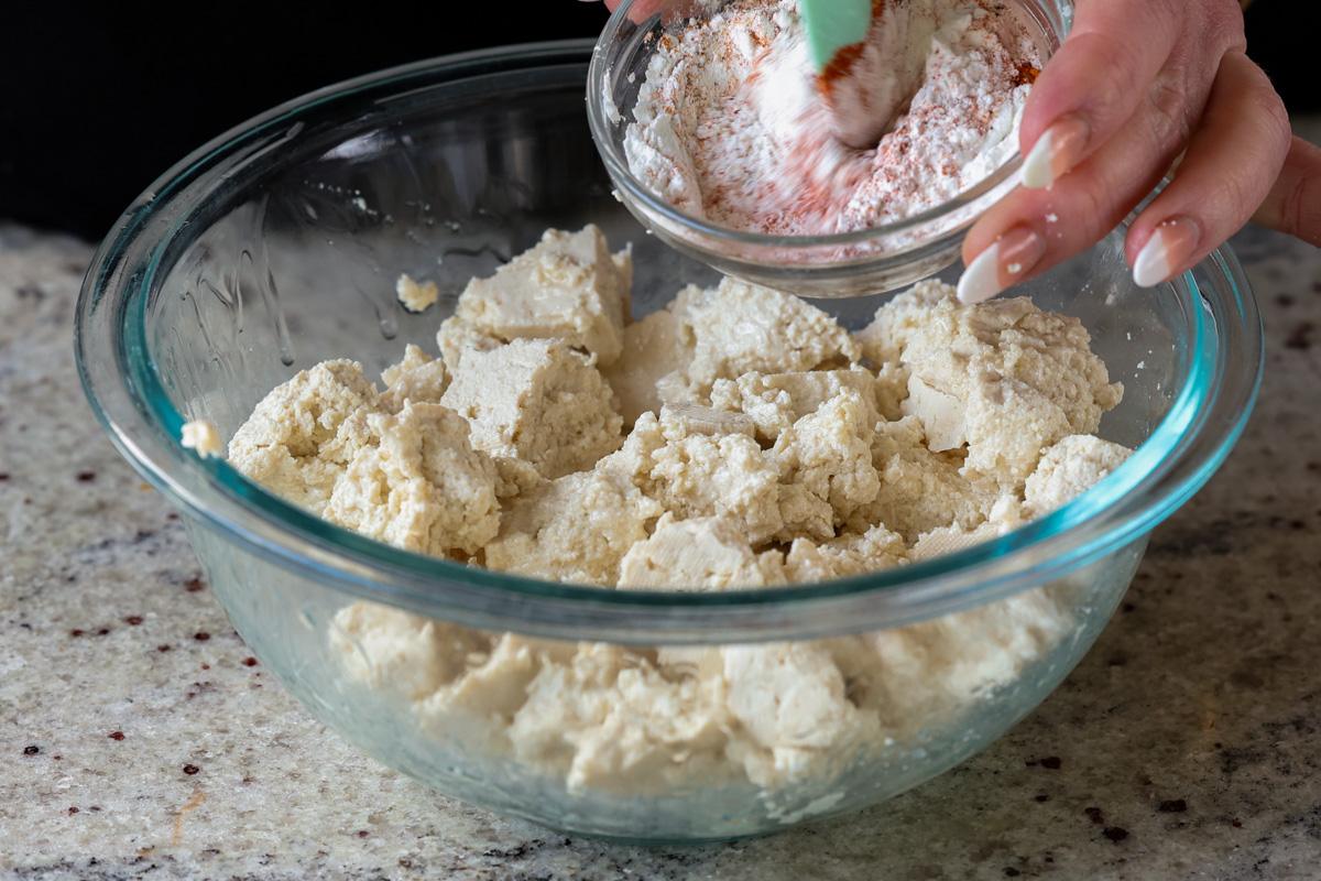 mixing cornstarch and spices over the bowl of tofu