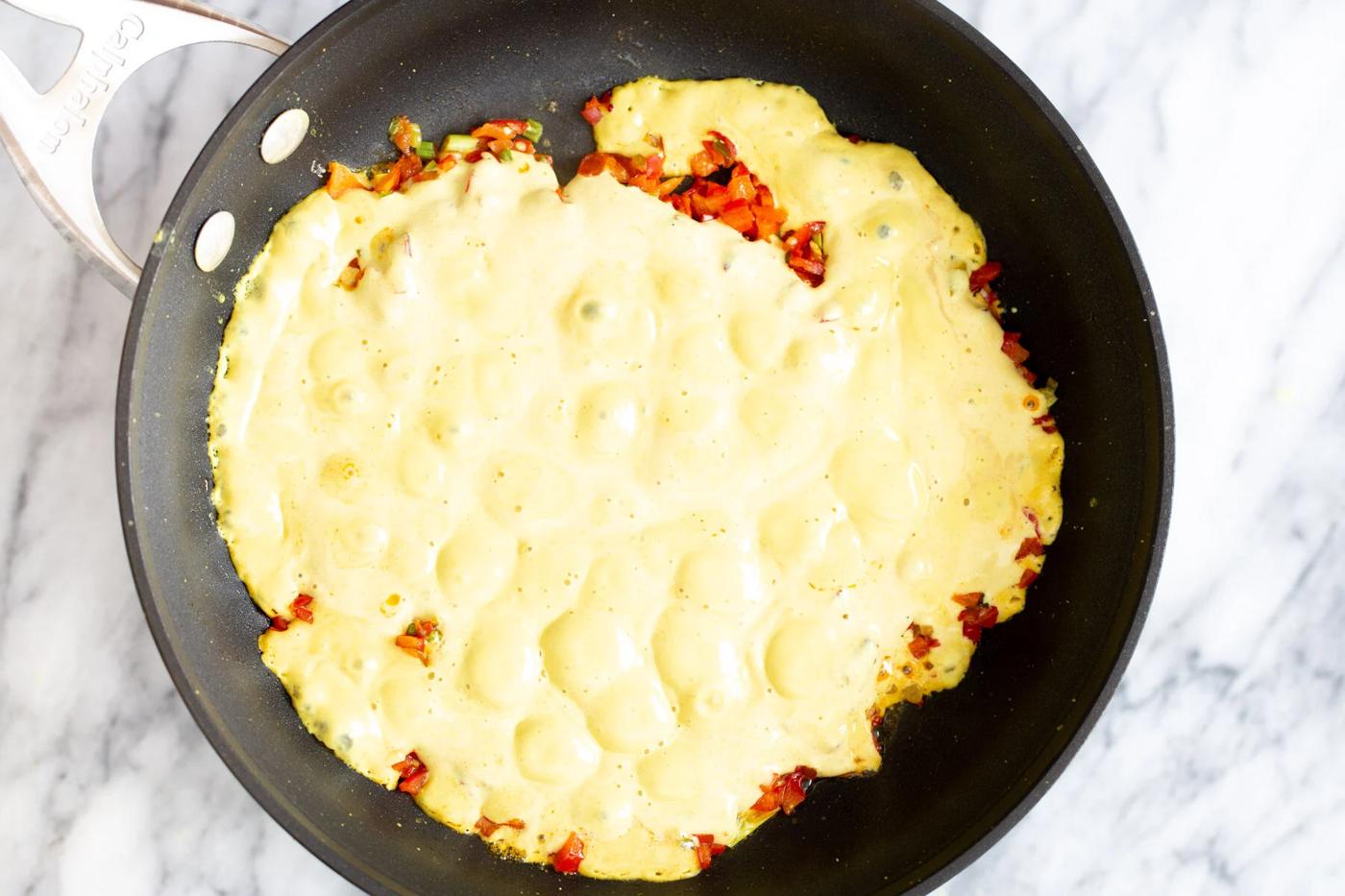 vegan tofu egg mixture being poured in a pan with sauteed vegetables