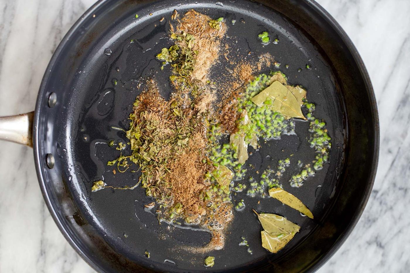 spices, bay leaf and chili in a black sauteeing pan