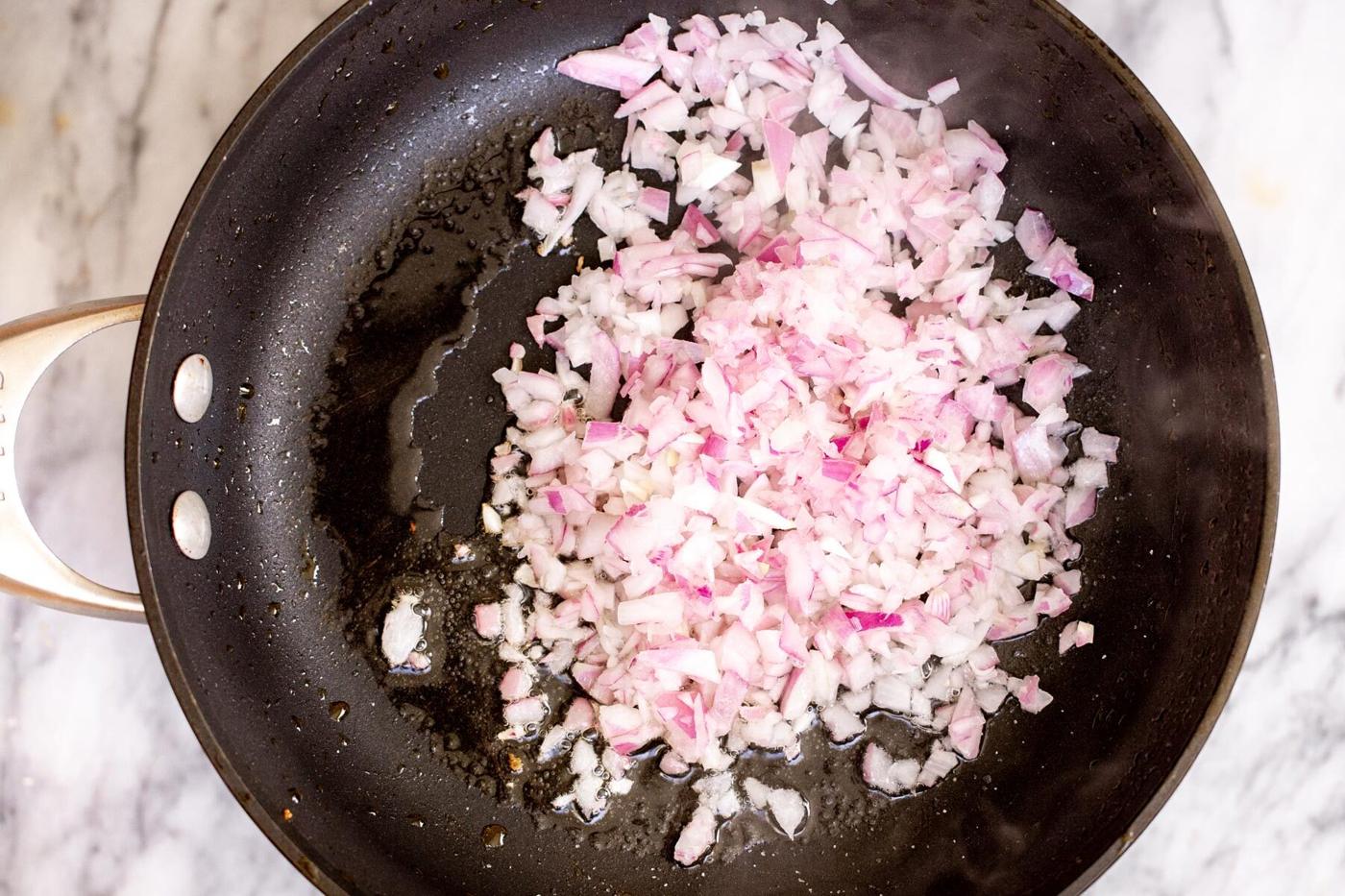 chopped red onions sauteeing in black sauteeing pan