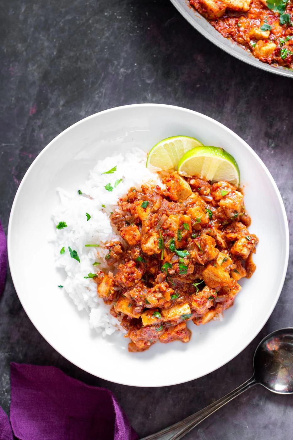 tofu vindaloo curry served with rice on a white plate with lime slices on the side