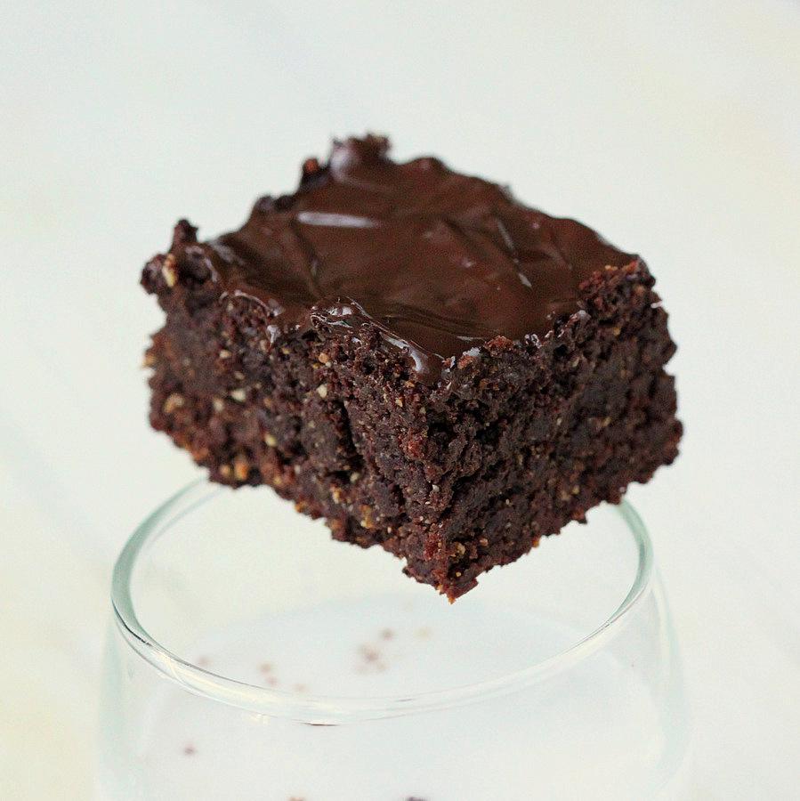 a small Vegan Triple Chocolate Salted Caramel Brownie balancing on the rim of a milk glass