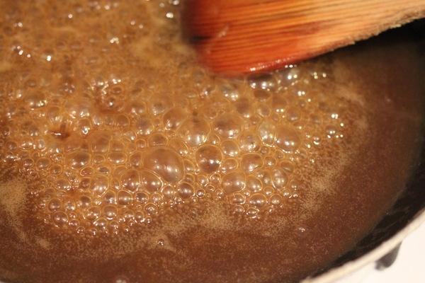 a wooden spoon stirring in a sauce pan with vegan salted caramel sauce