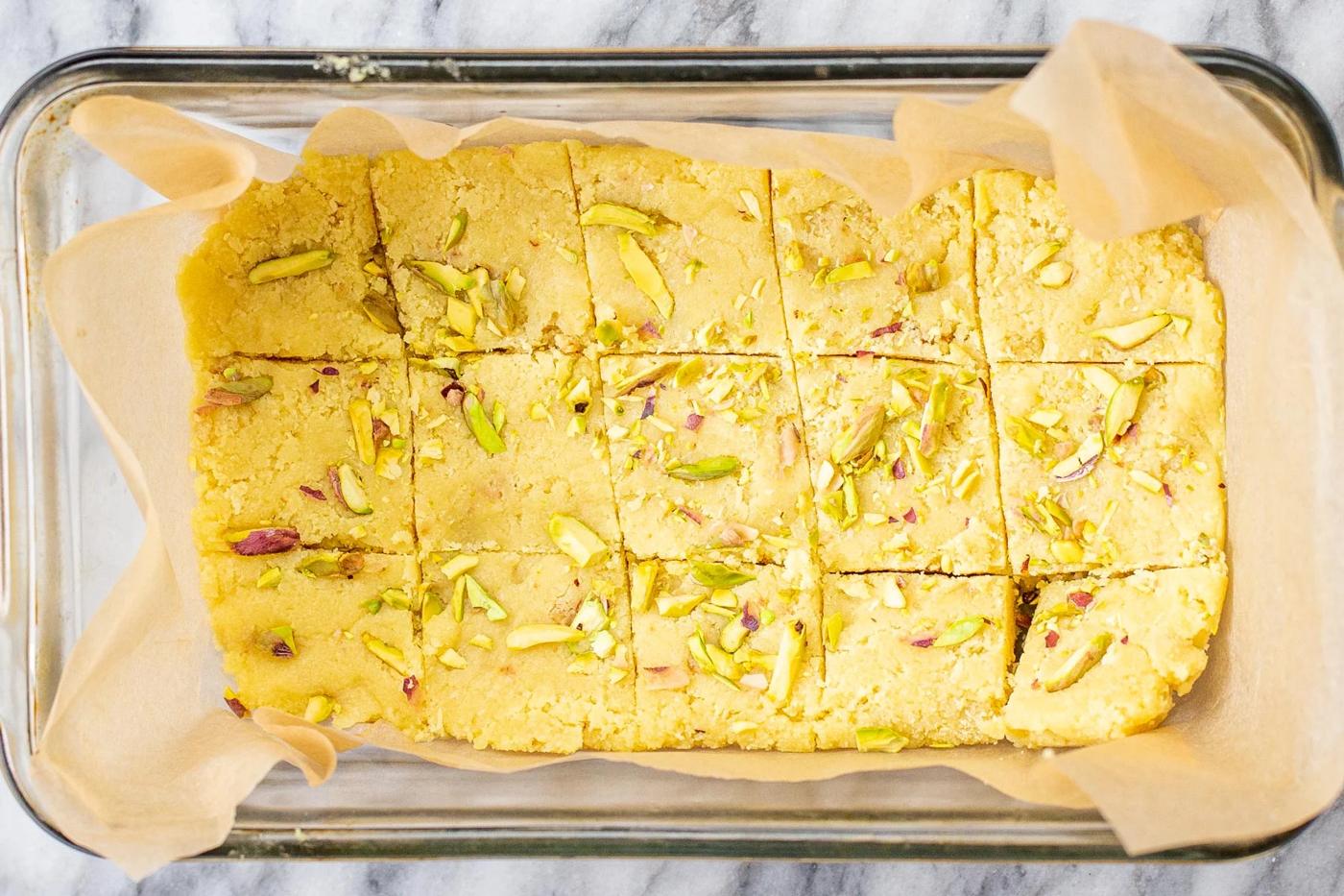 chilled almond burfi mixture being cut into squares in a pan