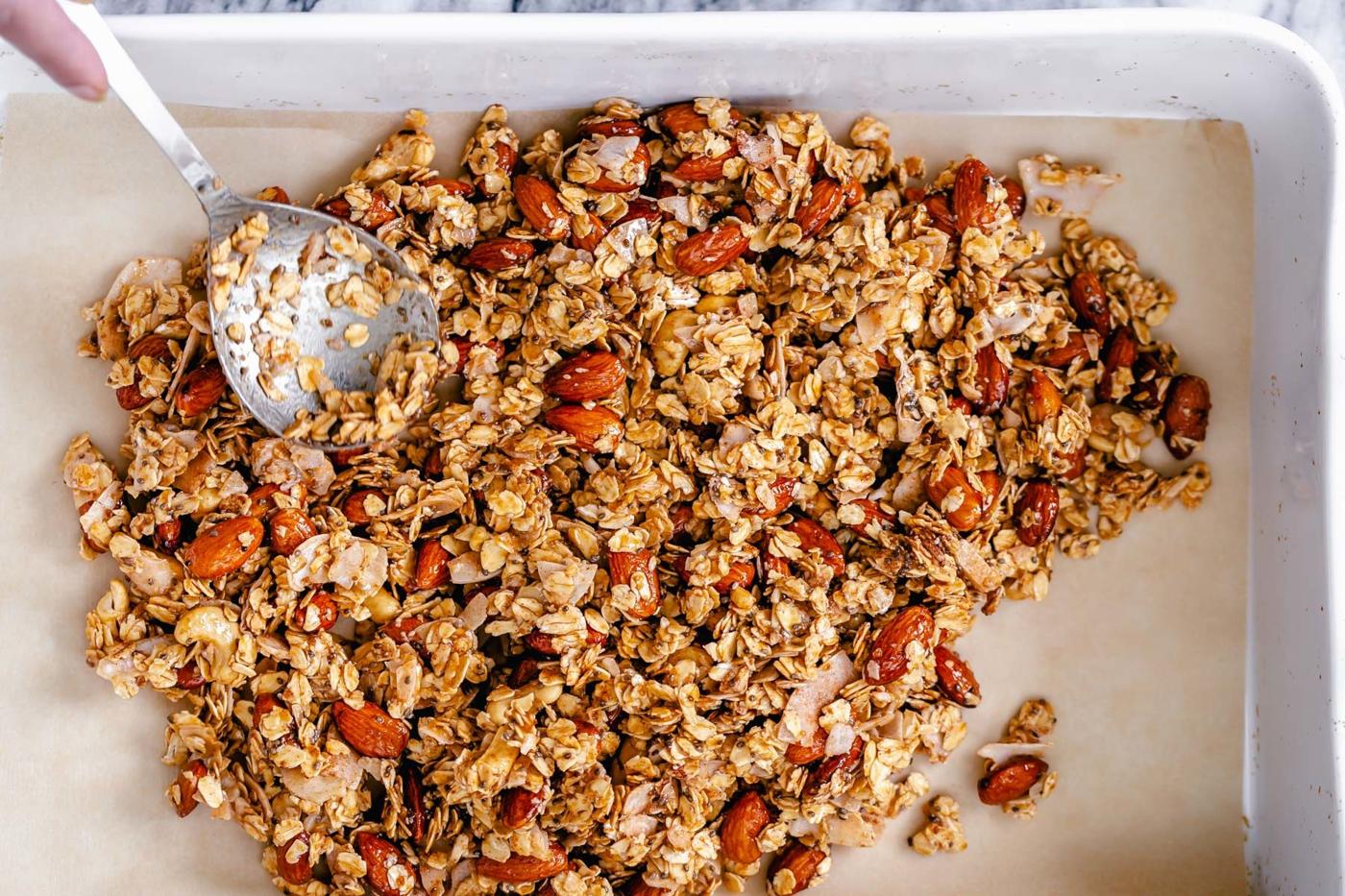 almond coconut granola being spread onto a baking tray to make baked vegan coconut granola