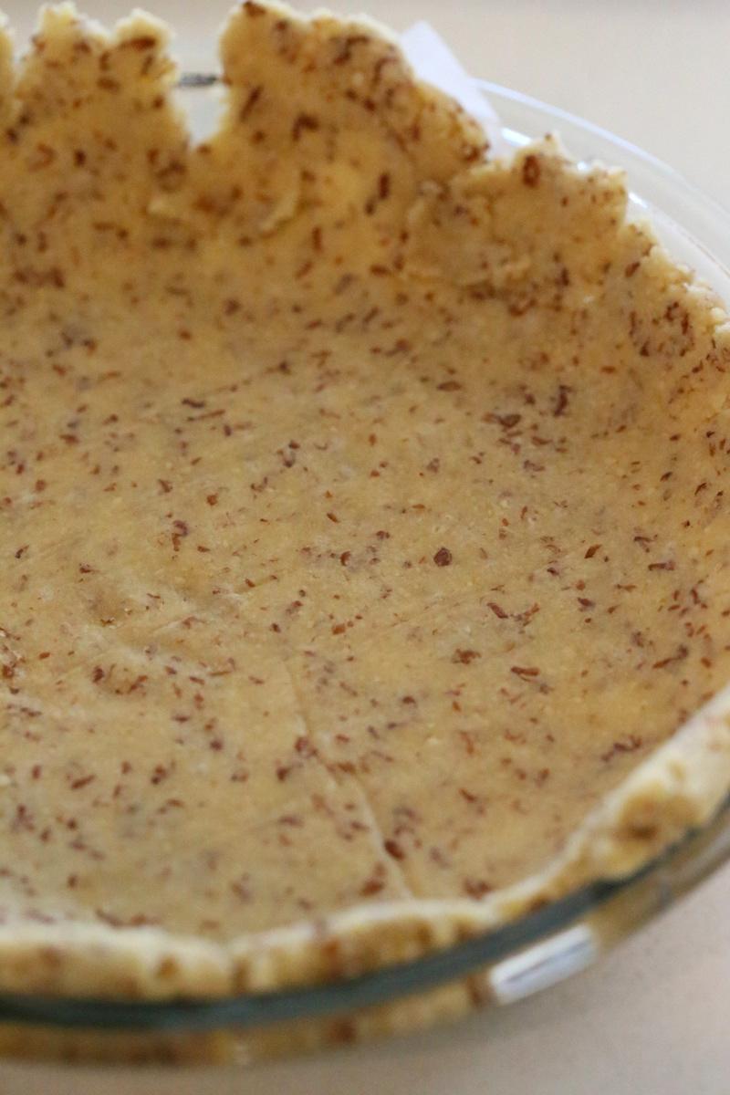 side view of a vegan gluten-free almond flour pie crust placed in a glass pie dish ready for baking